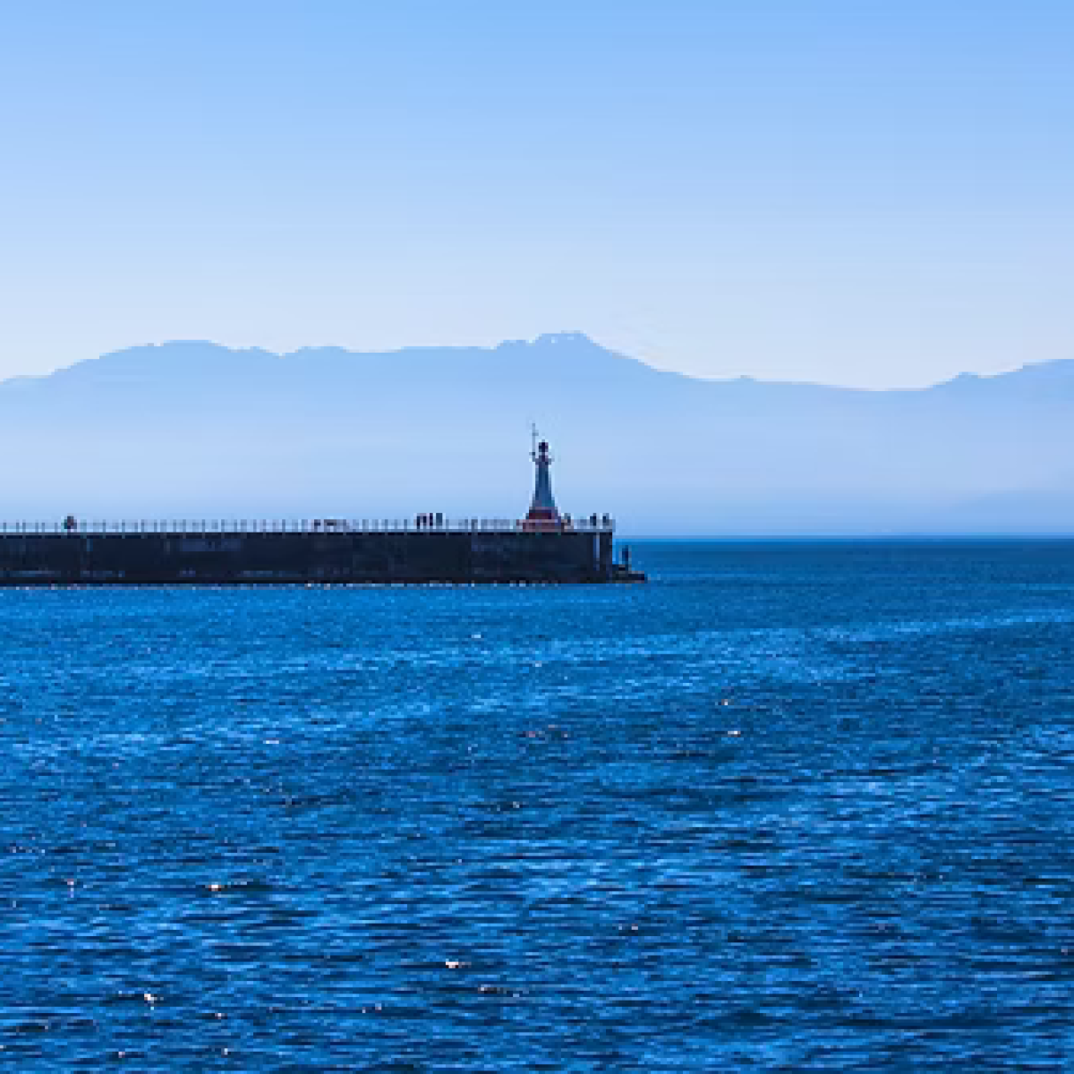 Blue ocean view with distant pier and mountains under clear sky.