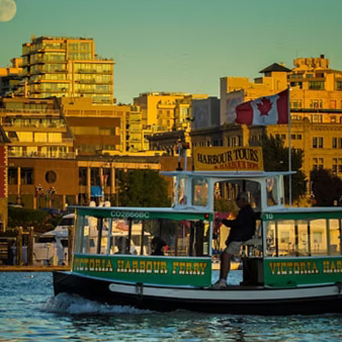 Ferry on water with city buildings and Canadian flag in the background.