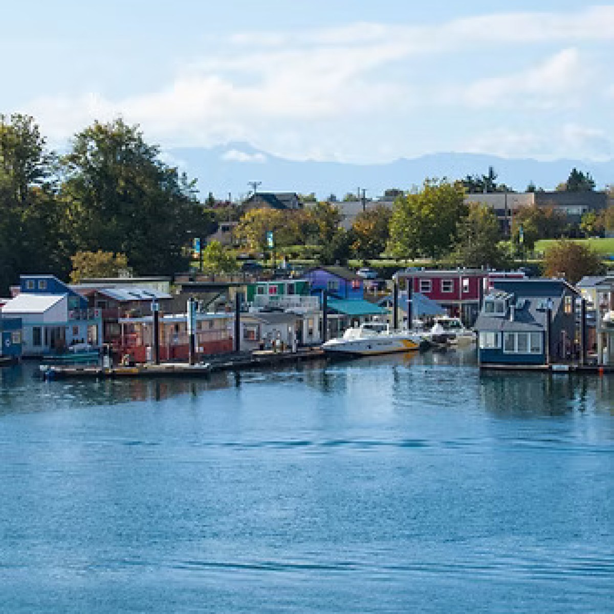 Colorful floating houses and boats on a calm harbor under a clear sky.