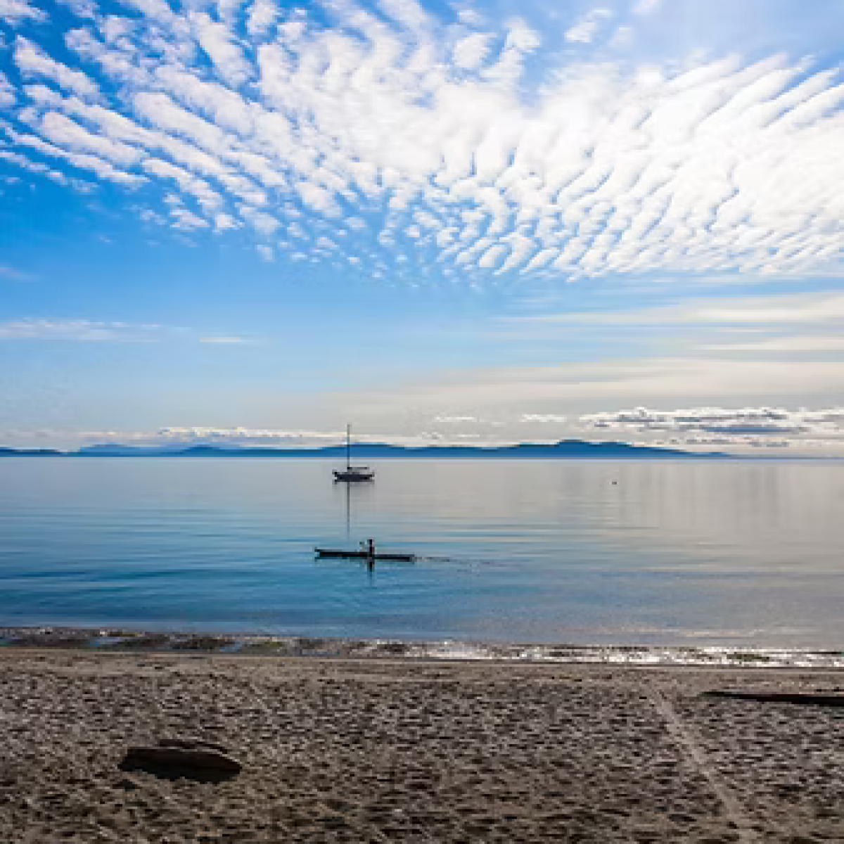 Calm beach with a lone boat and kayaker under a textured blue sky.